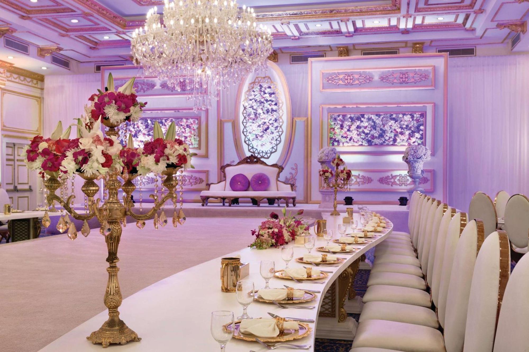 Grand Regency Doha, Trademark Collection By Wyndham מראה חיצוני תמונה The photo displays an elegantly decorated banquet or dining hall. It features a long, curved table set for a formal event, with fine china and floral centerpieces. Luxurious decorations include a grand chandelier hanging from the ceiling, and the wal