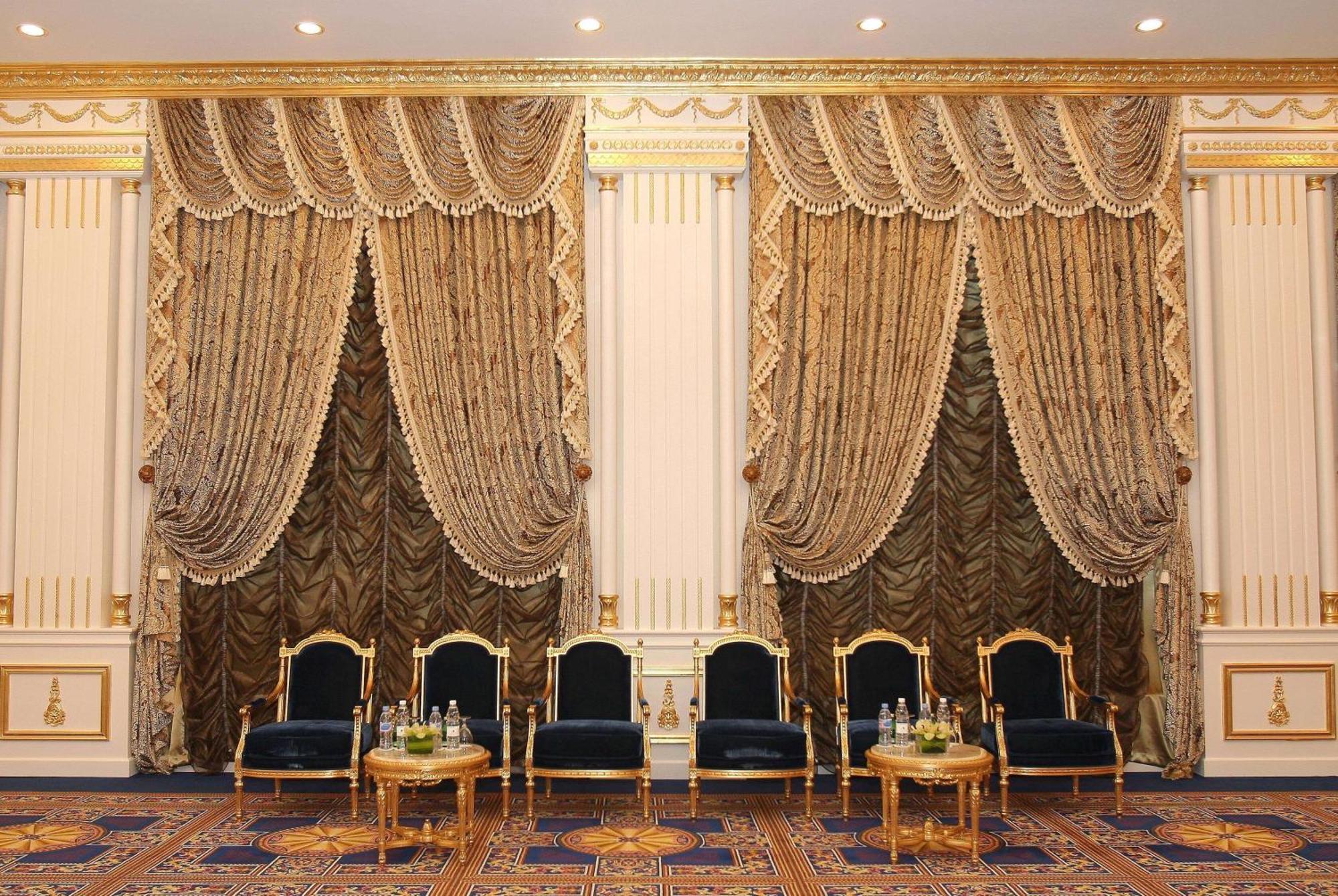 Grand Regency Doha, Trademark Collection By Wyndham מראה חיצוני תמונה The photo shows an elegantly decorated interior space. There are two sets of opulent curtains on the walls, featuring rich fabrics with ornate designs and gold accents. The curtains are paired with decorative tiebacks. In front of the curtains, there