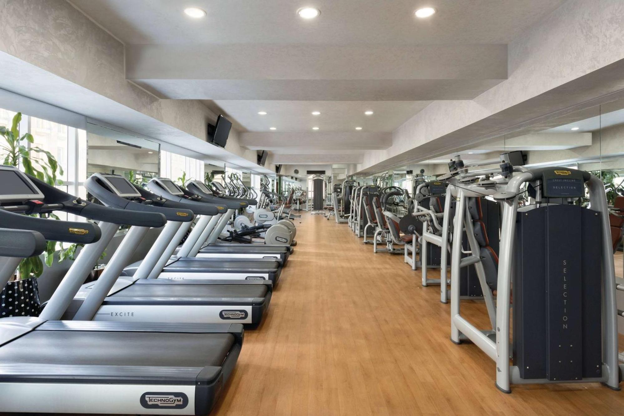 Grand Regency Doha, Trademark Collection By Wyndham מראה חיצוני תמונה The photo shows the interior of a gym or fitness center. It features a row of modern treadmills lined up against a wall, with a polished wooden floor. The space is brightly lit with recessed ceiling lights, and there are large mirrors on the walls, e