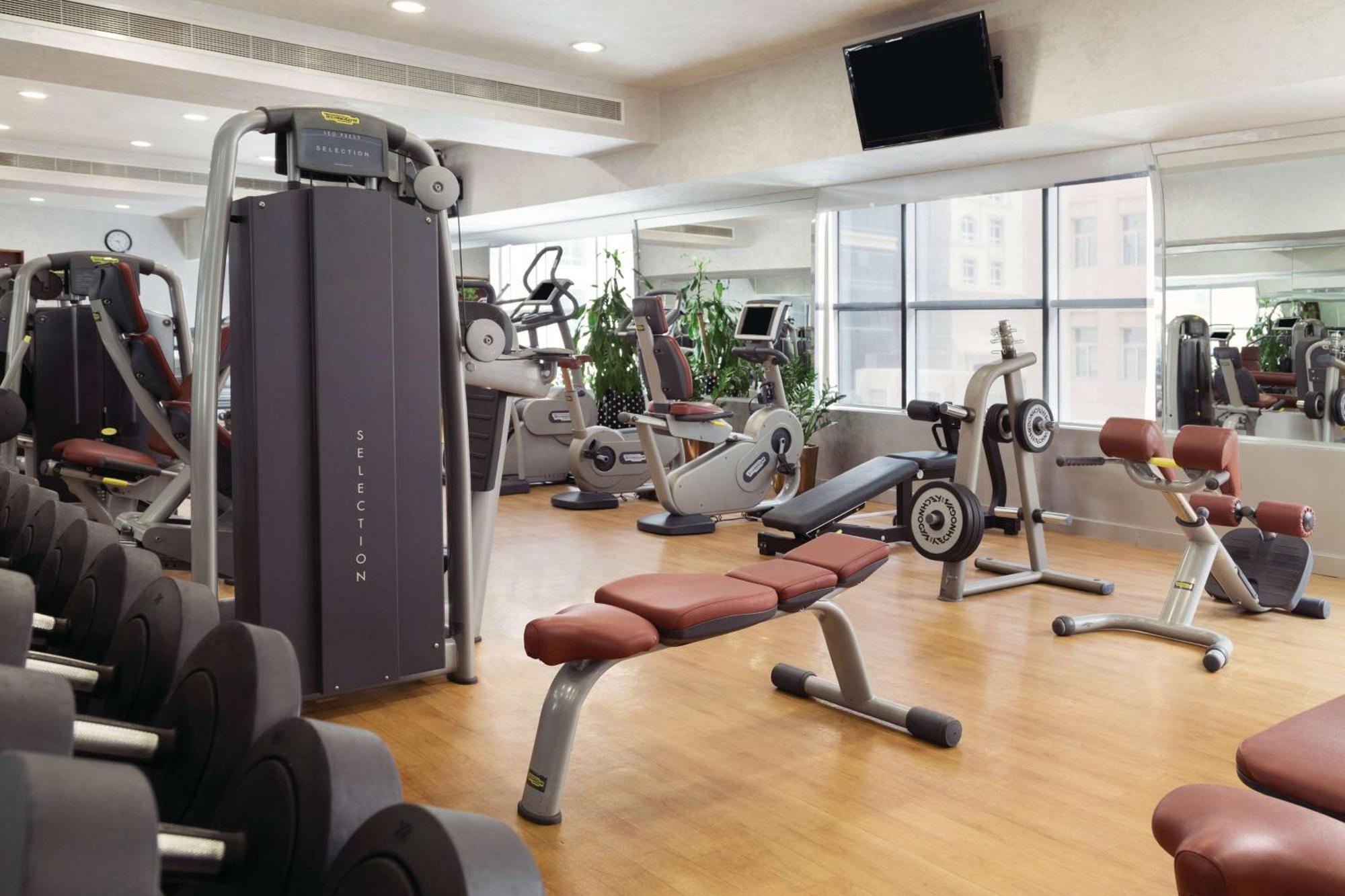 Grand Regency Doha, Trademark Collection By Wyndham מראה חיצוני תמונה The photo shows a fitness gym with various exercise equipment. There are weight machines, benches, and cardio machines such as stationary bikes and treadmills. The space has large windows allowing natural light to enter, and there are mirrors on the 