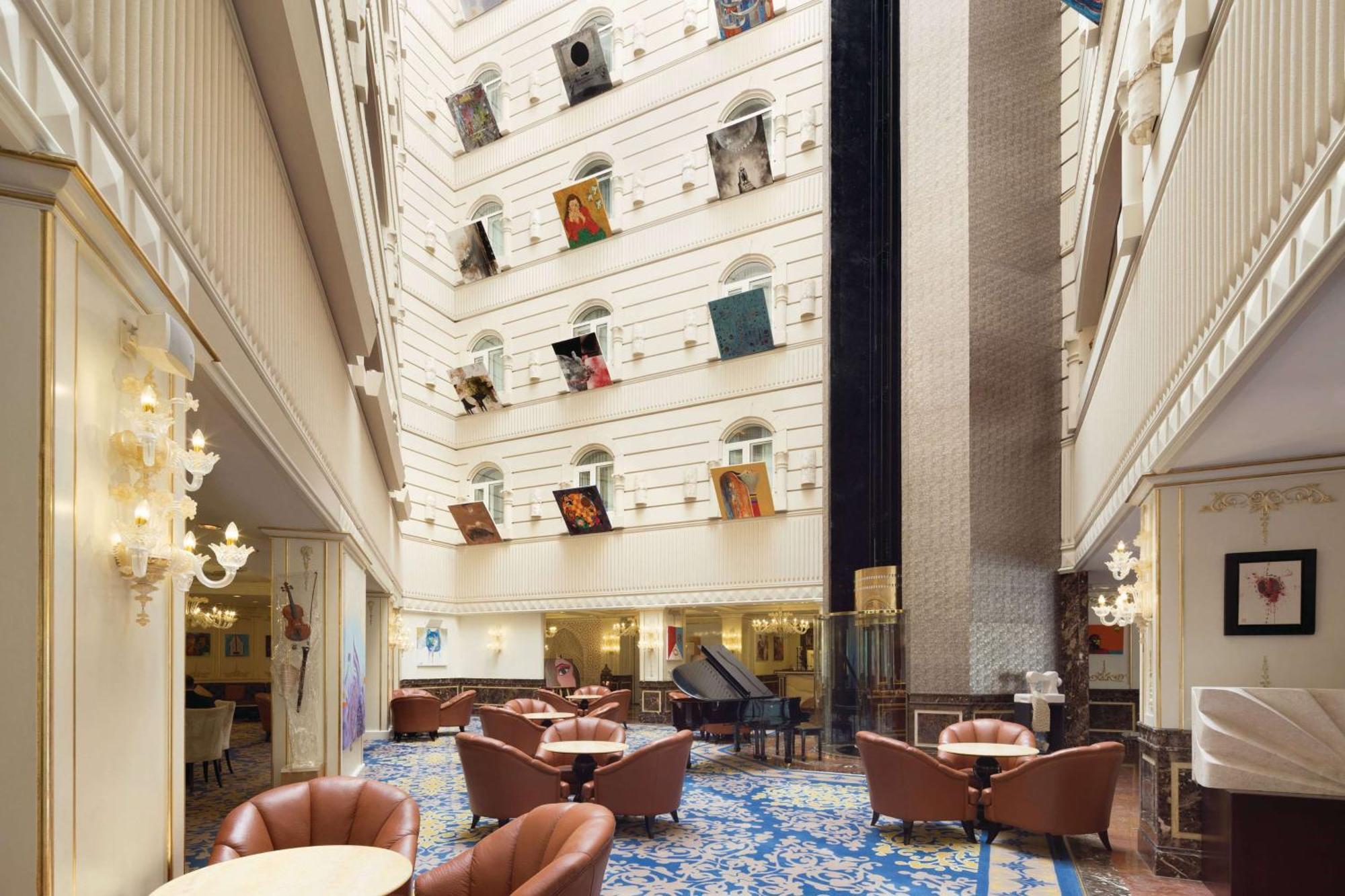 Grand Regency Doha, Trademark Collection By Wyndham מראה חיצוני תמונה The photo depicts the interior of a spacious, upscale hotel lobby. The design features high ceilings and multiple levels, with large windows that create a bright and airy atmosphere. Elegant light fixtures adorn the walls, and the floor is covered wi
