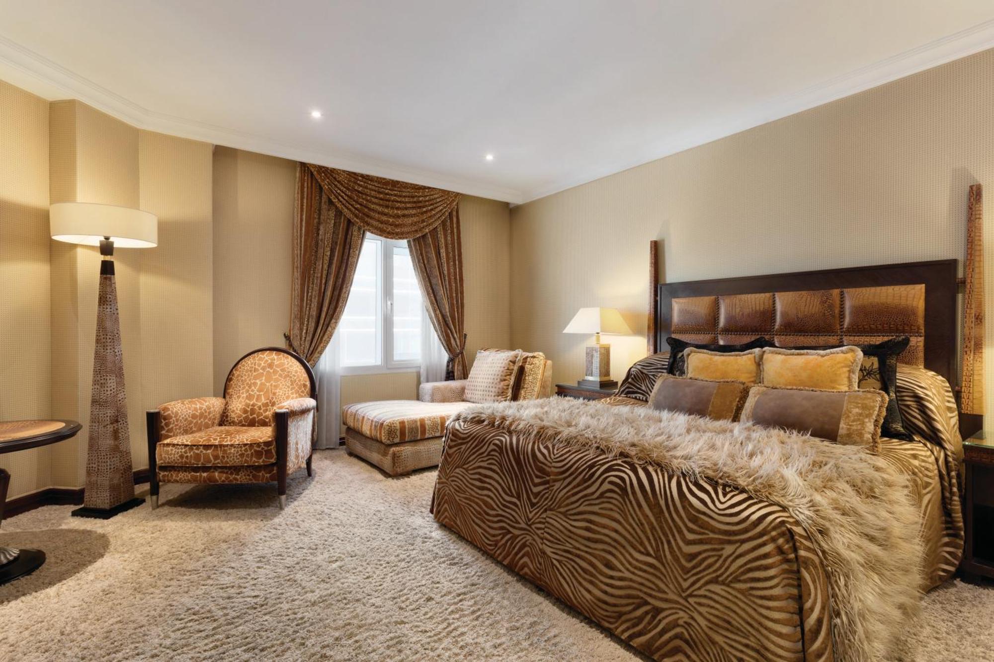 Grand Regency Doha, Trademark Collection By Wyndham מראה חיצוני תמונה The photo shows a stylishly decorated bedroom. The focal point is a large bed dressed in fabrics with a rich, textured appearance, possibly featuring a zebra print or similar design. On either side of the bed, there are small bedside lamps. 

Adjacen