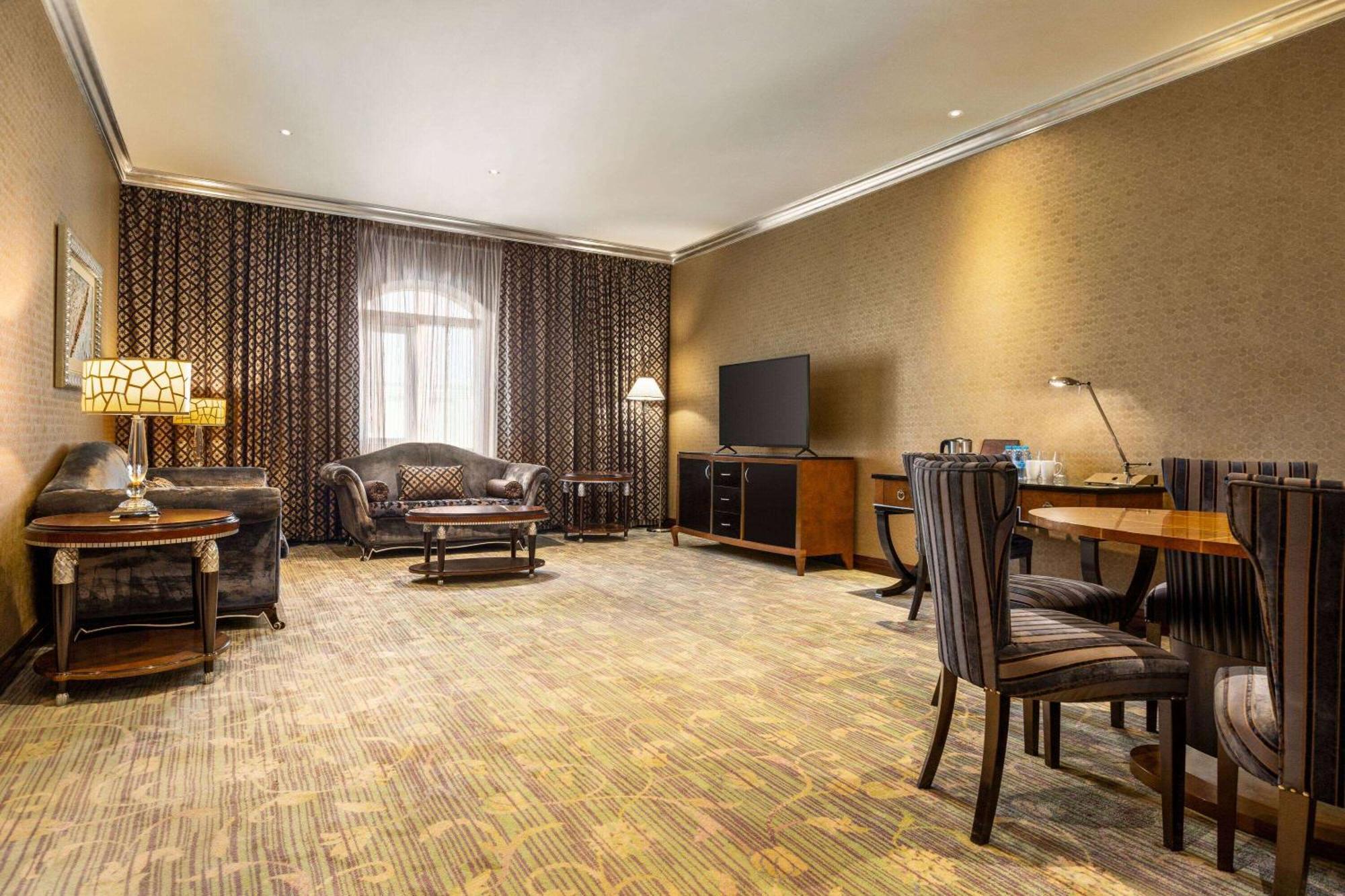Grand Regency Doha, Trademark Collection By Wyndham מראה חיצוני תמונה The photo shows a spacious lounge or living area. It features a comfortable seating arrangement with a dark-colored sofa and armchairs, arranged around a coffee table. There's a dining table with matching chairs, suggesting it can accommodate meals o